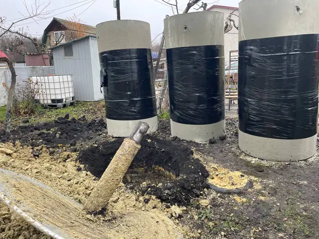 Три бетонных кольца, обмотанные плёнкой, стоят на участке рядом с будущим колодцем