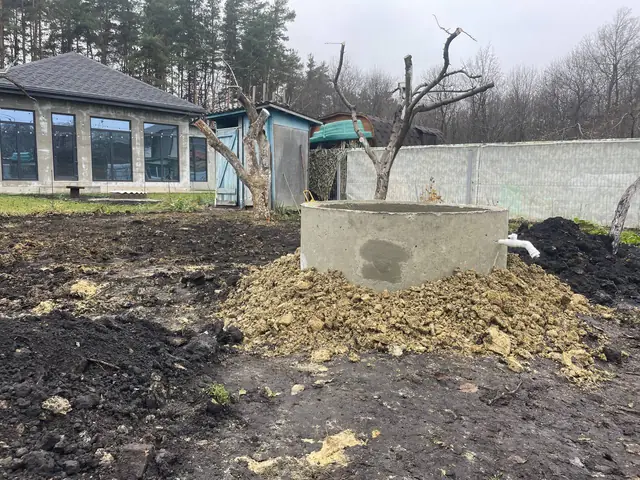 Готовый колодец из бетонных колец на участке, рядом отвал вынутого грунта